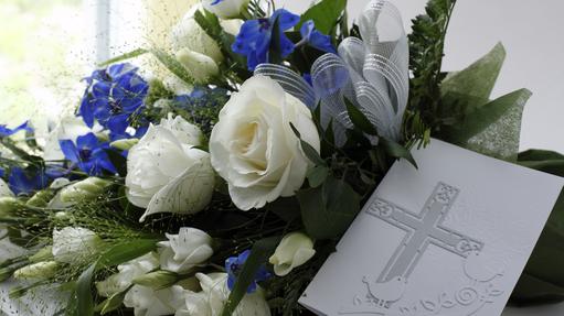 Blumenarrangement mit weißen Rosen und blauen Blüten, kombiniert mit einer tiefen Karte mit gekreuztem Motiv.