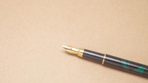 Nahaufnahme einer Füllfeder mit goldener Spitze auf einer braunen, strukturierten Unterlage.